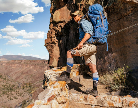 Man wearing Sockwell compression socks hiking in mountains with a fly fishing rod wearing a backpack