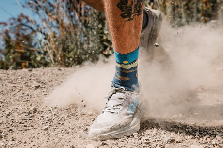 Person running on a dirt path with colorful socks and dusty sneakers.