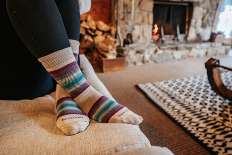 Feet wearing Sockwell socks on a couch in front of a fireplace