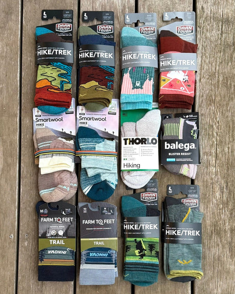 Collection of hiking and trekking socks in various designs and brands on a wooden surface.