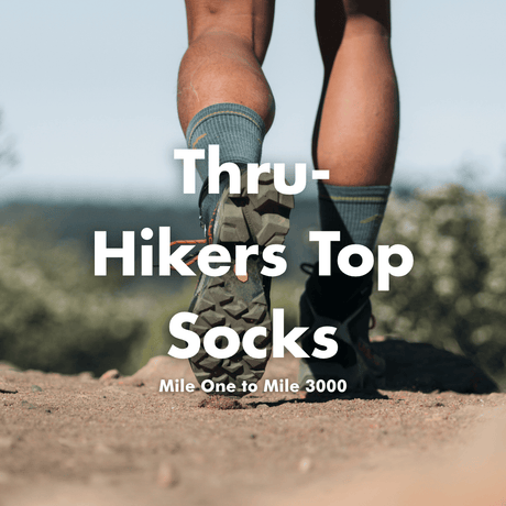 A close-up outdoor photo of a hiker's legs from behind, wearing hiking socks and trail shoes on a dirt trail. Large white text overlays read 'Thru-Hikers Top Socks' with smaller text 'Mile One to Mile 3000'.